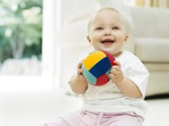 Baby sitting holding a multi colored ball | Infants playing with a soft ball can help improve motor skills.
